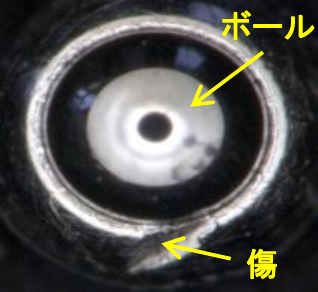 ペン先を拡大した顕微鏡写真。中央のボールと、ボール保持部に付いたキズを矢印で示している